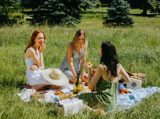 There is a group of women in dresses having a picnic in a field.